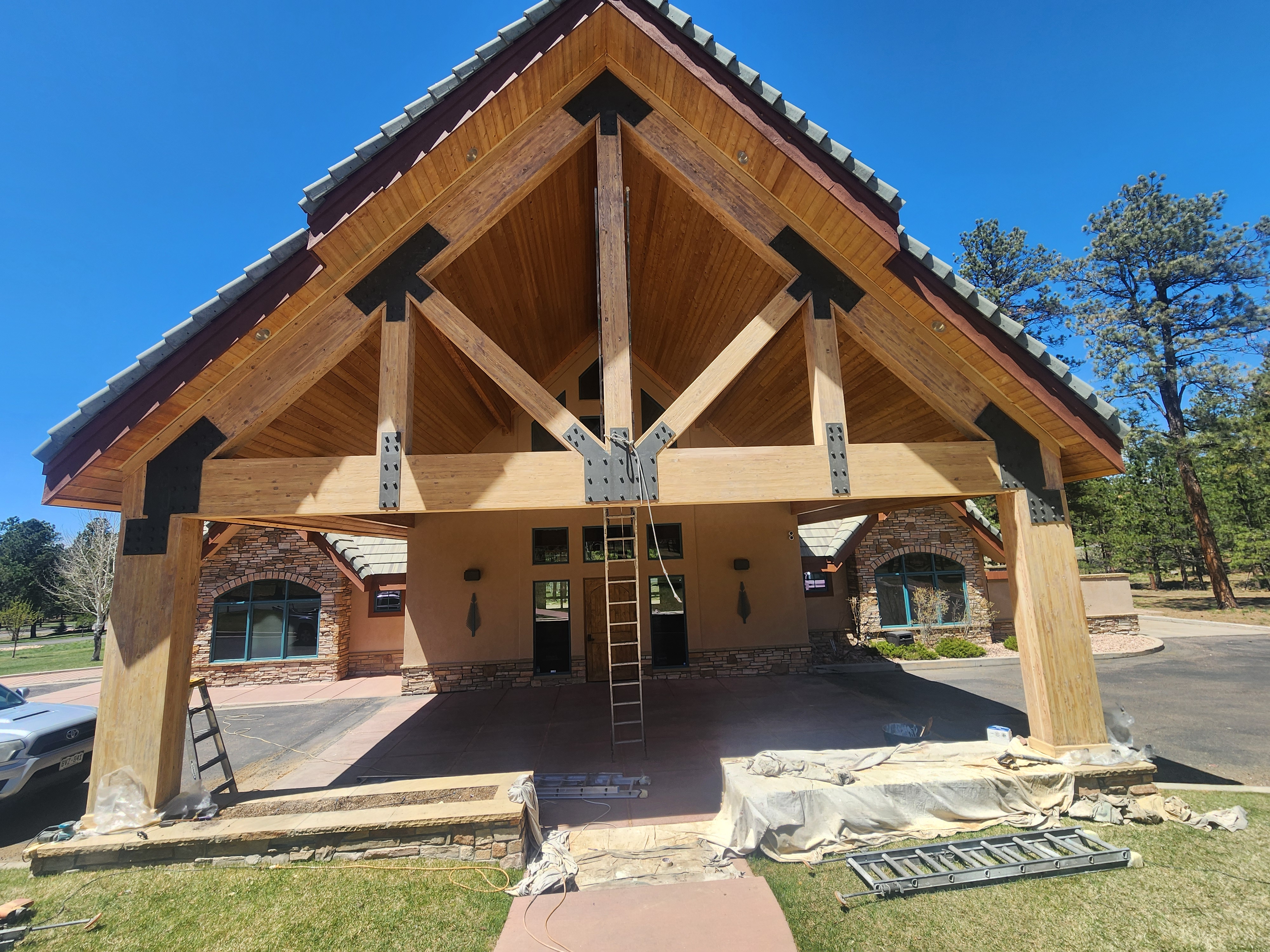 Lodge exterior varnish. Image of A-frame wood exterior awning being varnished. Blue skies and green trees.